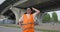 Worker with thick graying mustache in orange visibility and reflective safety vest idles in the middle of working day