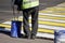 A worker in uniform is putting yellow and white paint on a pedestrian crossing sign. Life in the city