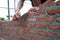 Worker uses the trowel for installing the red bricks on the wall