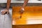 Worker varnishing lacquer on wooden floor outdoors by paint brush.