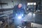 A Worker, welder in work clothes, construction gloves and a welding mask is welded with a welding machine metal product table,