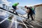 Workers building solar panel system on roof of house. Installers carrying photovoltaic solar module