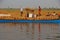 Workers carrying heavy gunny sack of harvested rice on their head onto the long blue boat to be transported