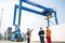 Workers discussing against large crane loading container at shipping yard