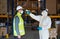 Workers with face mask and suit in warehouse, coronavirus and temperature measuring concept.