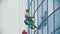 Workers hanging on ropes and wipes the exterior windows of a business skyscraper - attaching a device on the glass -