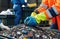 Workers in high-visibility clothing sort through recyclable materials in an industrial recycling facility