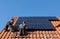 Workers installing solar electric panels on a house roof in Ochojno