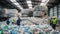 Workers observing large piles of plastic waste in a recycling plant