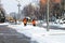 Workers in orange vests and a tractor clean the city street from fresh snow in the winter . Dnipro city