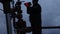 Workers in overalls and hard hats are carrying out repairs and maintenance of an oil well. Silhouette on the background