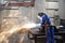 Workers in protective equipment in a foundry work on a casting with a grinding machine at the workplace