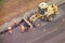 Workers with shovels in their hands remove asphalt from the road and putting it in the bucket of a bulldozer, top view