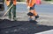 Workers in uniform throw shovels of asphalt on the road.