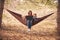 Working away from office concept, woman with two kids working on laptop while lying in hammock in a forest