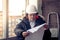 Working engineer in a white construction helmet with a project or drawing plan on the background of an industrial plant