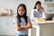 Working mom doing online job, her offended daughter feeling lonely, standing in kitchen interior, selective focus