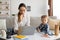 Working mother concept. Young lady typing on laptop keyboard while her toddler son drawing with pencils