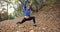 Working out in the park. Young woman in blue jacket gets ready for running stretching her arms and legs in beautiful