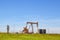 Working Pump Jack on oil well with tanks on site out on the horizon on the plains with electric lines and blue sky in background