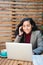 Working Remotely in Style: Young, Smiling Brunette Latina Professional at a Patio Cafe with Laptop and Phone