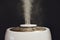 A working white humidifier on a black background, water vapor close-u