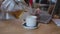 working woman cafe pouring hot tea from transparent teapot into white cup, drink