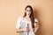 Working woman in glasses holding laptop and coffee, looking excited, hear amazing news, standing on beige background