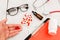 Workplace of doctor. Pills in hand, red stethoscope, clipboard and glasses on white wooden table