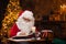 Workplace of Santa Claus. Cheerful Santa is reading the book of wishes while sitting at the table. Fireplace and
