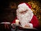 Workplace of Santa Claus. Cheerful Santa is reading the book of wishes while sitting at the table. Fireplace and