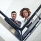 Works more fun from way up here. Low angle portrait of two coworkers leaning on a stairwell bannister.