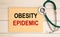 Worksheet with the inscription OBESITY EPIDEMIC and stethoscope