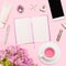 Workspace with diary, pen, smartphone, lipstick, alstroemerias, tea cup, cosmetics tube on pastel pink background.