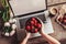 Workspace with girl`s hands, laptop computer, bouquet of peonies flowers, coffee, strawberries, smartphone on rough wooden table.