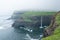 World famous Mulafossur waterfall falling from the cliff near Gasadalur village into the ocean in Faroe Islands . Misty, cloudy