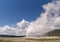 The world famous Old Faithful Geyser erupts in Yellowstone National Park on a beautiful, sunny summer day with a sky full of