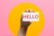 World hello day. Raised female hand with a card with the inscription Hello. Pink background with a yellow circle