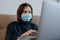 World pandemic. Woman with protective mask on her face isolating at home, reading last news about coronavirus from laptop. Social