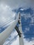 Worm's eye view of a white triangular bridge with suspension cables crisscrossing a blue and cloudy sky