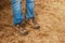 Worn and dirty work shoes with bluejeans scrunched at top with worn and stained knees - cropped legs of man standing on straw and