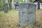 A worn sandstone grave marker in the shade on a very bright day. There is no text visible on the stone, but there is some moss on