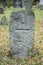 A worn sandstone grave marker in the shade on a very bright day. There is no text visible on the stone, but there is some moss on