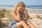 Worried blond girl on the beach sitting on the sand