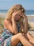 Worried blond girl on the beach sitting on the sand