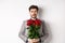 Worried boyfriend in suit, holding flowers roses and looking doubtful at camera, standing with bouquet on valentines day
