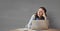 Worried business woman at a desk using a computer against grey background