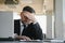 Worried businessman in dark suit sitting at office desk full with books and papers being overloaded with work.