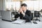 Worried businessman in dark suit sitting at office desk full with books and papers being overloaded with work.