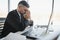 Worried businessman in dark suit sitting at office desk full with books and papers being overloaded with work.